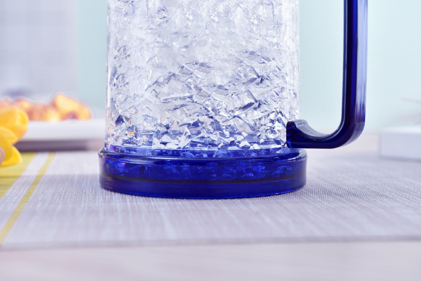 Clear glass mug with blue handle filled with ice cubes on a light surface.